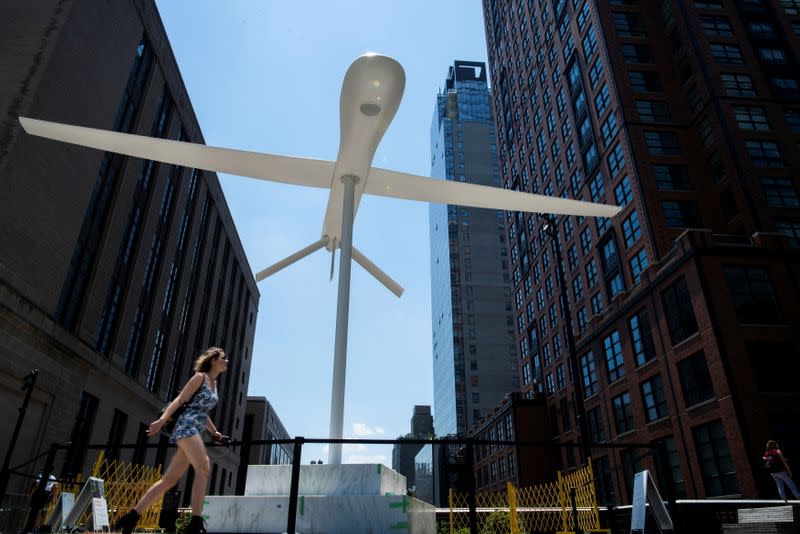 A woman walks near a sculpture by artist Sam Durant "Untitled" (drone), a fiberglass sculpture depicting a Predator drone, as it is seen over the High Line park in Manhattan borough of New York