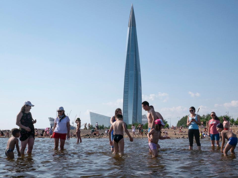 People bathe on a beach at the Gulf of Finland in St.Petersburg, Russia, Saturday, July 27, 2019, with the business tower Lakhta Centre, the headquarters of Russian gas monopoly Gazprom, in the background.