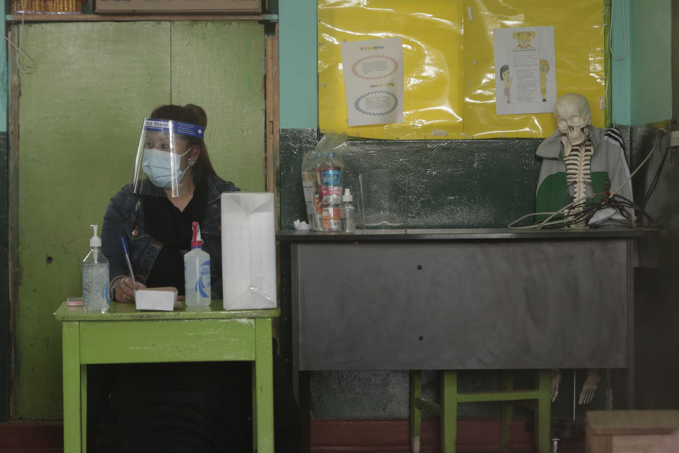 Wearing a mask and face shield, an electoral official waits for voters at a school being used as a polling station during general elections in Cuzco, Peru, Sunday, April 11, 2021. Peruvians went to the polls amid a surge in new COVID-19 infections. (AP Photo/Sharon Castellanos)