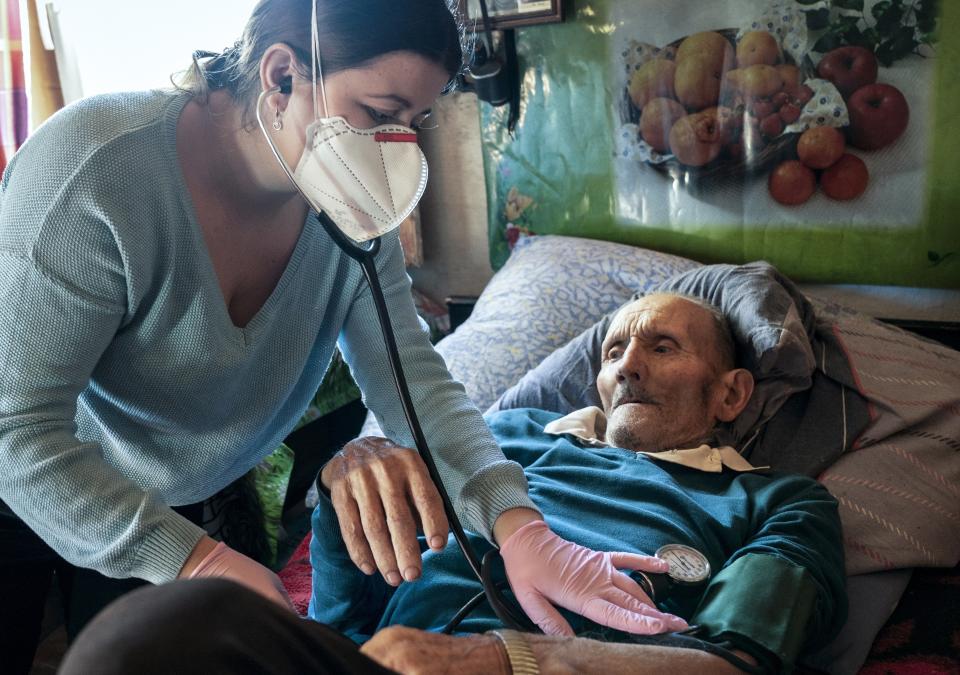 Dr. Viktoria Mahnych, wearing face mask against coronavirus, checks on a COVID-19 patient with a stethoscope at at his home in Iltsi village, Ivano-Frankivsk region of Western Ukraine, Wednesday, Jan. 6, 2021. Mahnych fears that a lockdown in Ukraine came too late and the long holidays, during which Ukrainians frequented entertainment venues, attended festive parties and crowded church services, will trigger a surge in new coronavirus infections. (AP Photo/Evgeniy Maloletka)