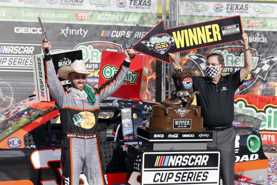 FILE - In this July 19, 2020, file photo, Texas Motor Speedway president and general manager Eddie Gossage, right, holds a "Winner" sign as Austin Dillon, left, celebrates by firing six-shooters after winning the NASCAR Cup Series auto race at Texas Motor Speedway in Fort Worth, Texas. NASCAR is providing quite a night to mark the 25th season of racing at Texas Motor Speedway, and sendoff for track president and showman Eddie Gossage, whose last race is Sunday after overseeing the track from its groundbreaking in 1995, two years before it opened. (AP Photo/Ray Carlin, File)