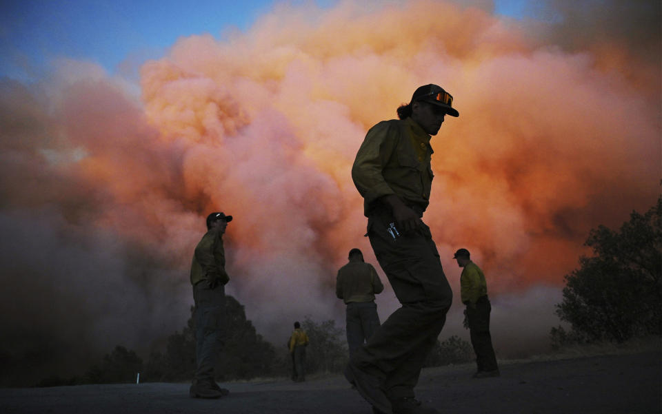 U.S. Forest firefighters stand along a road watching a wildfire burn.