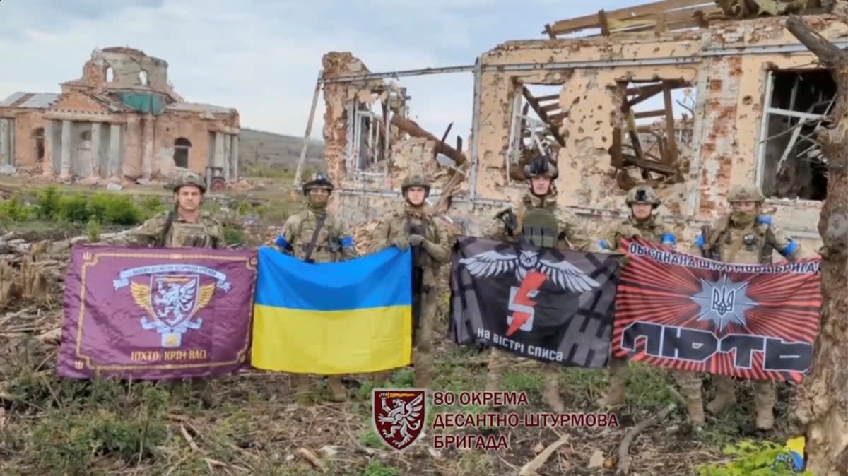 Soldiers hold flags as they speak in front of destroyed buildings in Klishchiivka (Col. Gen. Syrskyi via Reuters)