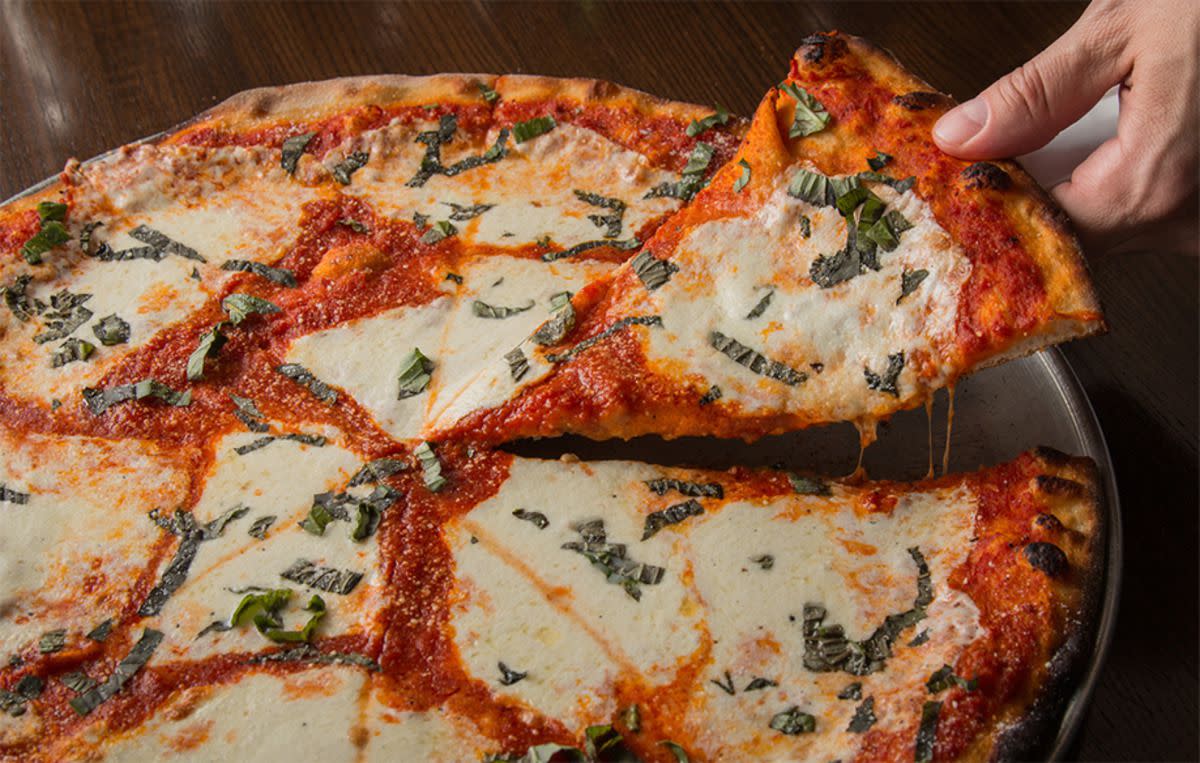 Margherita Pie on a serving plate, Denino’s, Staten Island, New York, a hand taking a piece, on a wooden table