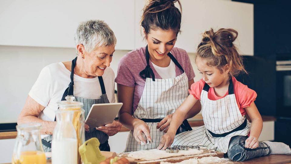 Different generations of women with digital tablet preparing cookies together.