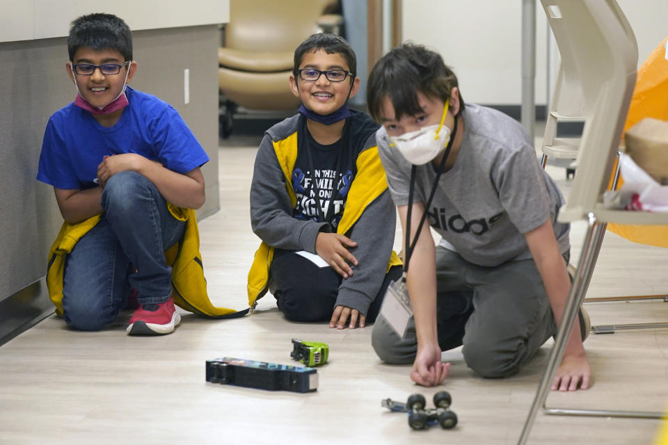 Ronan Kotiya, left, and his brother Keaton Kotiya, right, look on and smile after Alex Oliver pushed a toy car during a break in a workshop for young caregivers of ALS diagnosed family members in Dallas, Texas, Saturday, April 9, 2022. The children have gathered for a clinic to learn more about caring for people with Lou Gehrig's disease, or amyotrophic lateral sclerosis. It's a fatal illness that attacks nerve cells that control muscles throughout the body. (AP Photo/LM Otero)