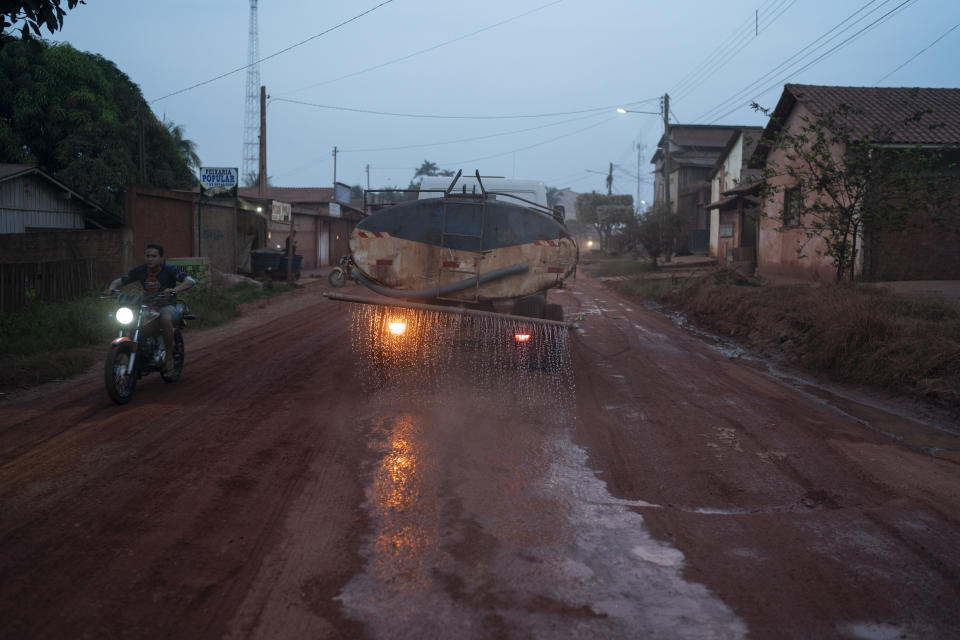 In this Nov. 29, 2019 photo, a tank truck pours water on the street at dusk in Ruropolis, Para state, Brazil. Carved through jungle during Brazil’s military dictatorship in the 1970s, the roads that meet in Ruropolis were built to bend nature to man’s will in the vast hinterland. (AP Photo/Leo Correa)