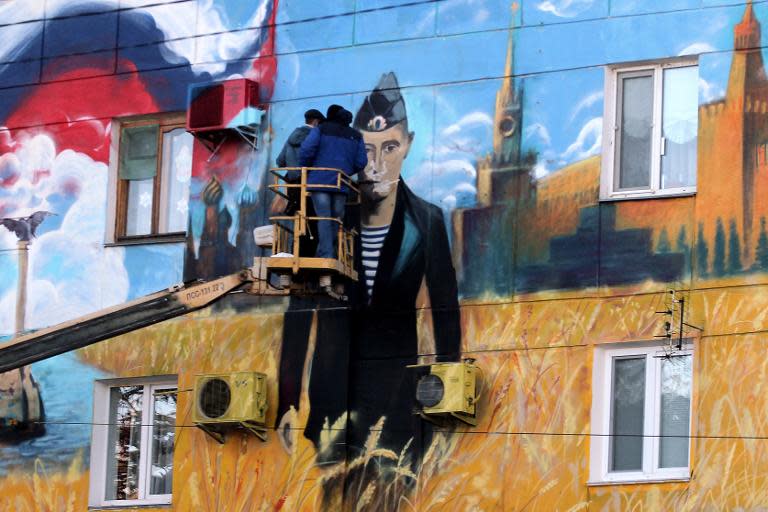 Workers stand on a crane in front of a mural depicting Russian President Vladimir Putin in a navy uniform, the Kremlin and the Russian flag on the wall of a building in the Crimean city of Sevastopol, on January 13, 2015