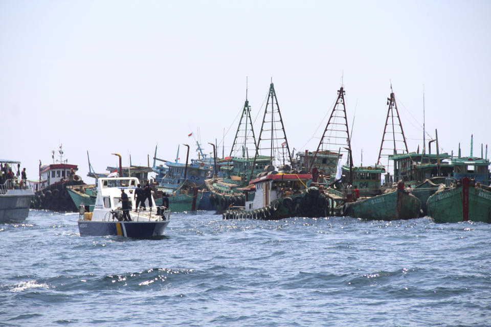 An Indonesian Maritime and Fisheries Ministry patrol boat sails past foreign fishing boats caught operating illegally in Indonesian waters before sinking them off Datuk Island, West Kalimantan, Indonesia, Saturday, May 4, 2019. Indonesian authorities have resumed its tough stance against poaching in the country's water by sinking 51 foreign ships. (AP Photo/William Pasaribu)