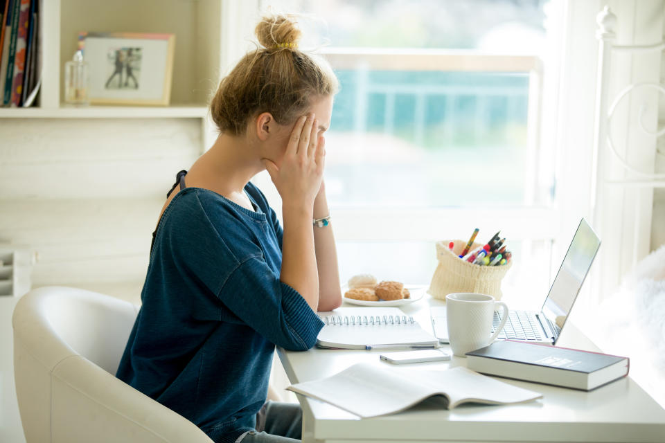 Portrait of an attractive woman in a chair at table with a laptop, book, notebook on it, hands at her temples. Concept photo