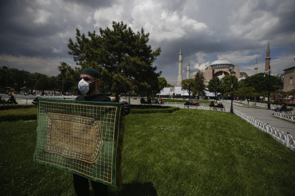 A Muslim man prepares his prayer mat at the plaza, backdropped by a ''wall' set in front of Istanbul's 6th-century Hagia Sophia, the main cathedral of the Byzantine Empire which was converted into a mosque with the Ottoman conquest of the city, then known as Constantinople, in 1453, that was to be used as a set for the celebrations to mark the 567th anniversary of the conquest in Istanbul, Friday, May 29, 2020. A Muslim cleric recited the "prayer of conquest" from the Quran inside the Hagia Sophia. Muslim prayers at the UNESCO World Heritage site are highly controversial, hitting at the heart of the country's religious-secular divide. (AP Photo/Emrah Gurel)