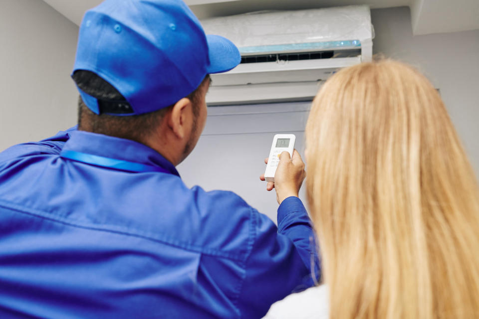 Service worker explaining female customer how use remote control to change temperature with air conditioner / Credit: Getty Images/iStockphoto