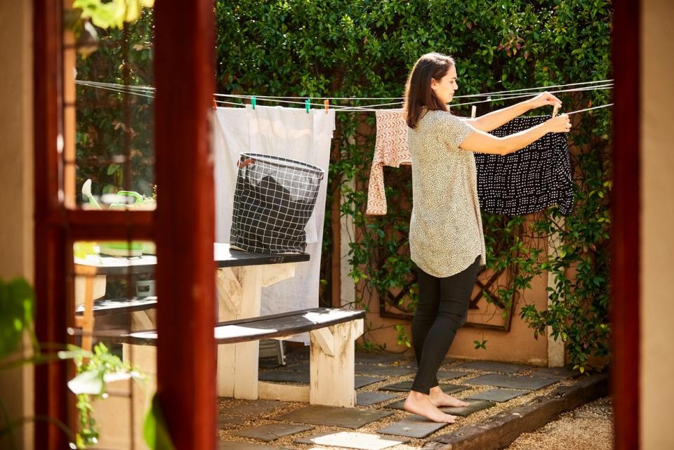 Woman hangs clothes on clothesline in backyard in bright morning light