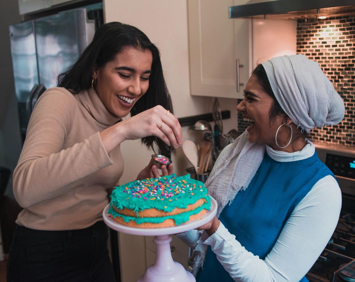 two friends laughing while putting sprinkles on a cake