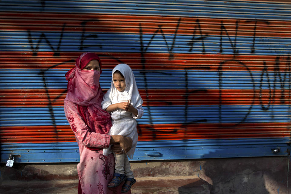 In this Sept. 27, 2019, photo, a Kashmiri woman protestor Jawahira Banoo carries her 3-year-old daughter Rutba and stands for a photograph outside a closed shop with a spray-painted graffiti after a protest on the outskirts of Srinagar, Indian controlled Kashmir. Banoo says she does not miss an opportunity to come out to the streets to protest. The men are at a higher risk of being detained, she says. (AP Photo/ Dar Yasin)