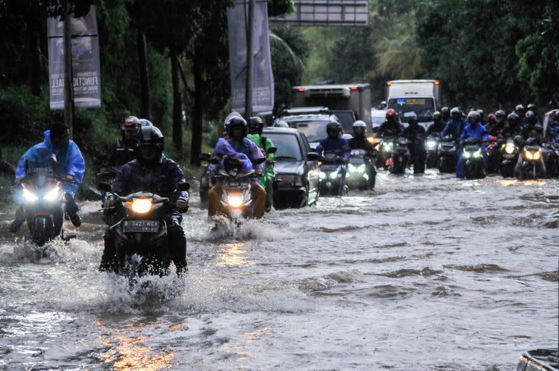 People ride motorcycles along a flooded street in Bekasi, near Jakarta