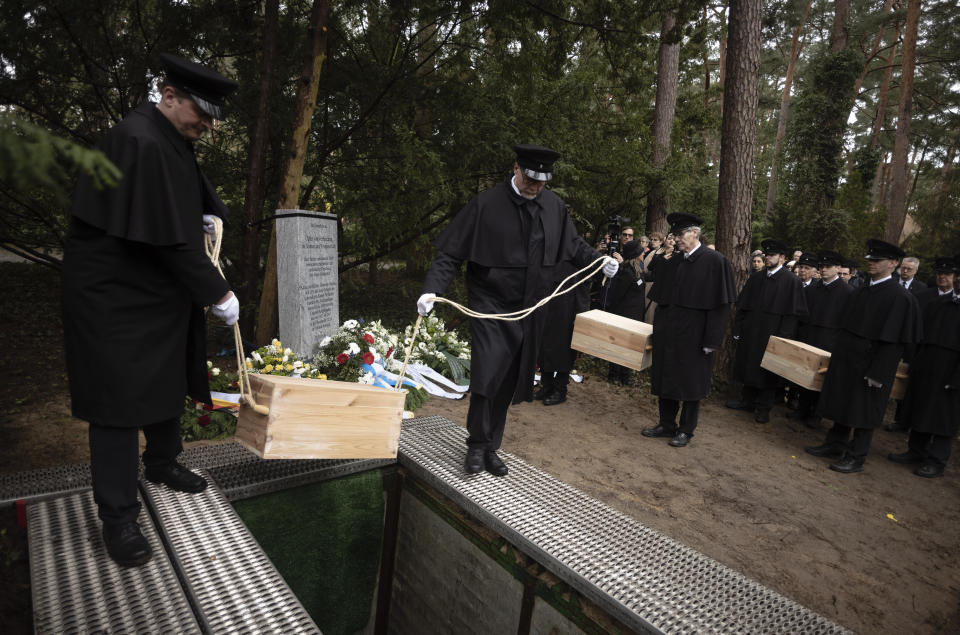 Caskets containing bones found on the grounds of the Freie Universitat, Free University are lowered into the ground for burial, at the Waldfriedhof in Berlin, Germany, Thursday, March 23, 2023. Thousands of bone fragments found in the grounds of a Berlin university where an institute for anthropology and eugenics was once located, which may include the remains of victims of Nazi crimes, were buried on Thursday. (AP Photo/Markus Schreiber)