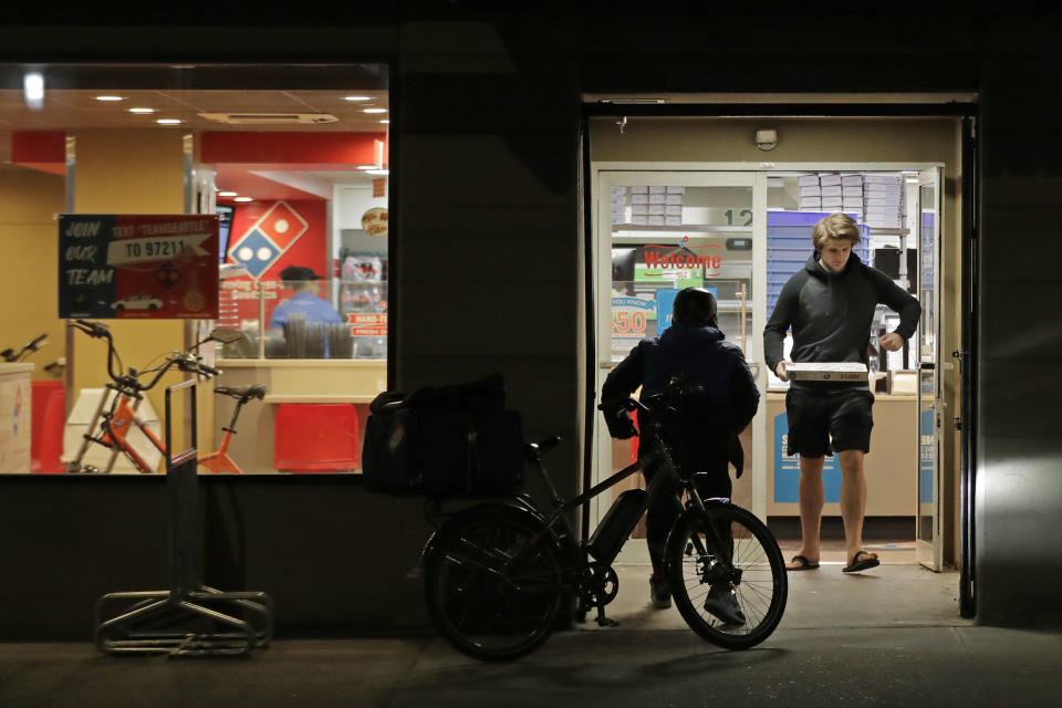 A man uses his elbow to open the door as he walks out of a Domino's Pizza restaurant in downtown Seattle as a delivery driver walks in, Sunday, March 15, 2020. Washington Gov. Jay Inslee said Sunday night that he would order all bars, restaurants, entertainment and recreation facilities in the state to temporarily close to fight the spread of the COVID-19 coronavirus. Inslee said that restaurants could continue take-out and delivery services. (AP Photo/Ted S. Warren)