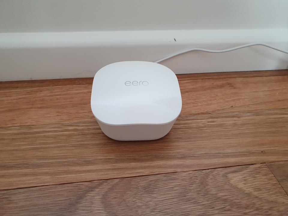 Amazon Eero wifi device sitting on a wooden floor.