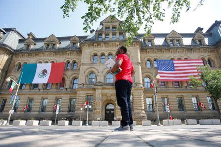 The Mexican and U.S. flags hang from the Langevin Block in advance of Wednesday's North American Leaders' Summit as a man waits for a bus by in Ottawa, Ontario, Canada, June 27, 2016. REUTERS/Chris Wattie