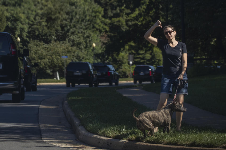 A resident walking her dog gestures as the motorcade of President Donald Trump drives by towards the Trump National Golf Club in Sterling, Va., Sunday, Aug. 30, 2020. (AP Photo/Manuel Balce Ceneta)