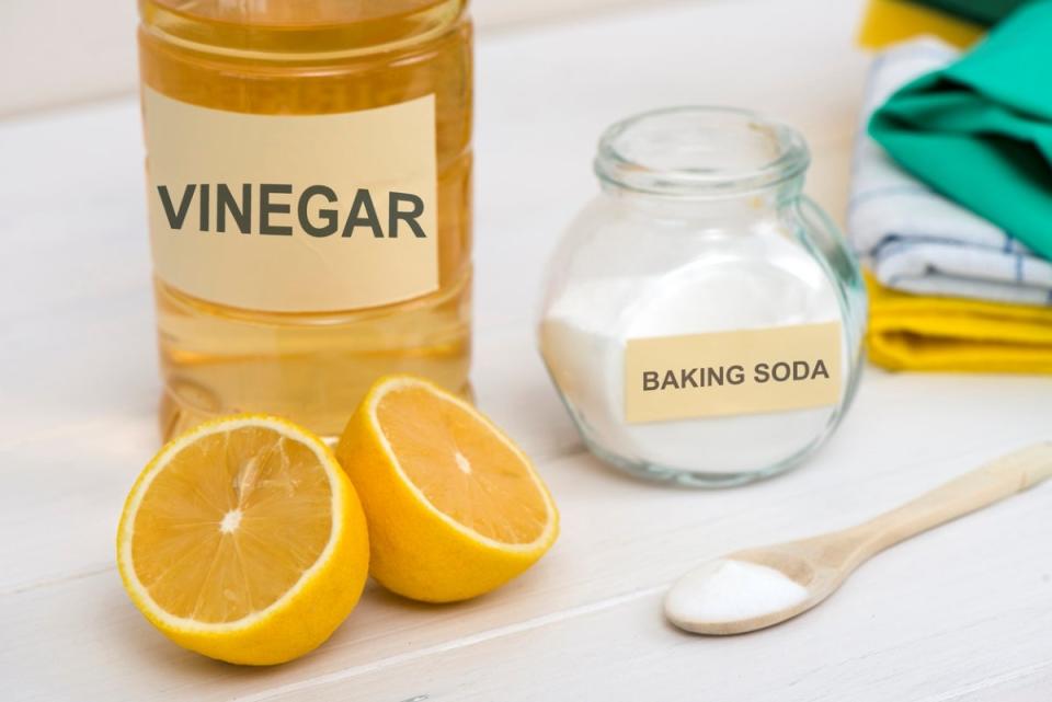 Labeled jars of vinegar and baking soda with cut lemon in foreground
