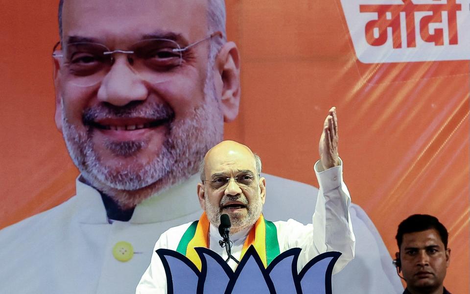 Mr Shah gestures from a podium in front of a large portrait of himself