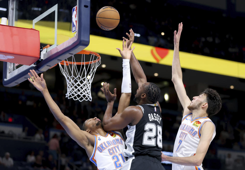 San Antonio Spurs center Charles Bassey (28) goes to the basket as Oklahoma City Thunder guard Aaron Wiggins (21) and forward Chet Holmgren (7) defend in the first half of a preseason NBA basketball game, Monday, Oct. 9, 2023, in Oklahoma City. (AP Photo/Sarah Phipps)