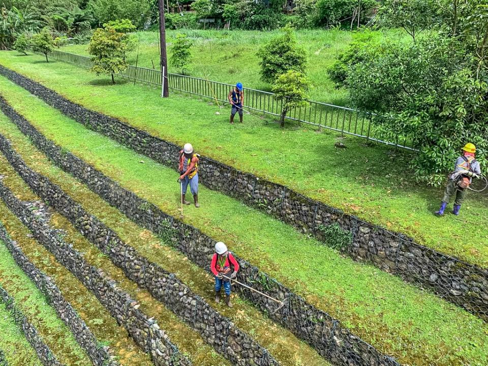 《圖說》工作人員揹著除草機站在層層堆疊的石籠護岸執行除草工作。〈水利局提供〉