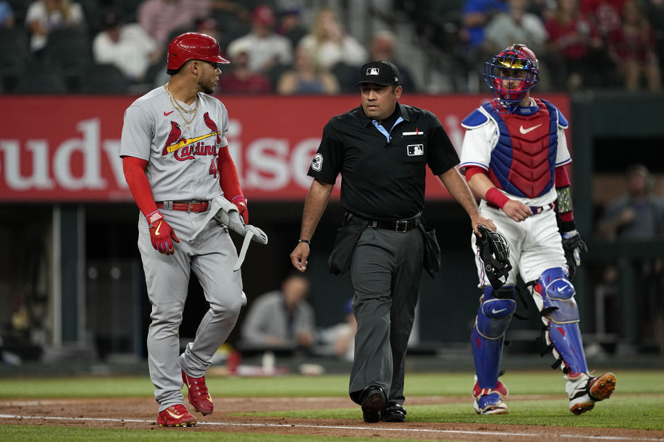 St. Louis Cardinals' Willson Contreras, left, and Texas Rangers' Mitch Garver, right, walk beside umpire Nestor Ceja, center, as Contreras walks to first after being hit by a pitch during the first inning of a baseball game Tuesday, June 6, 2023, in Arlington, Texas. (AP Photo/Tony Gutierrez)