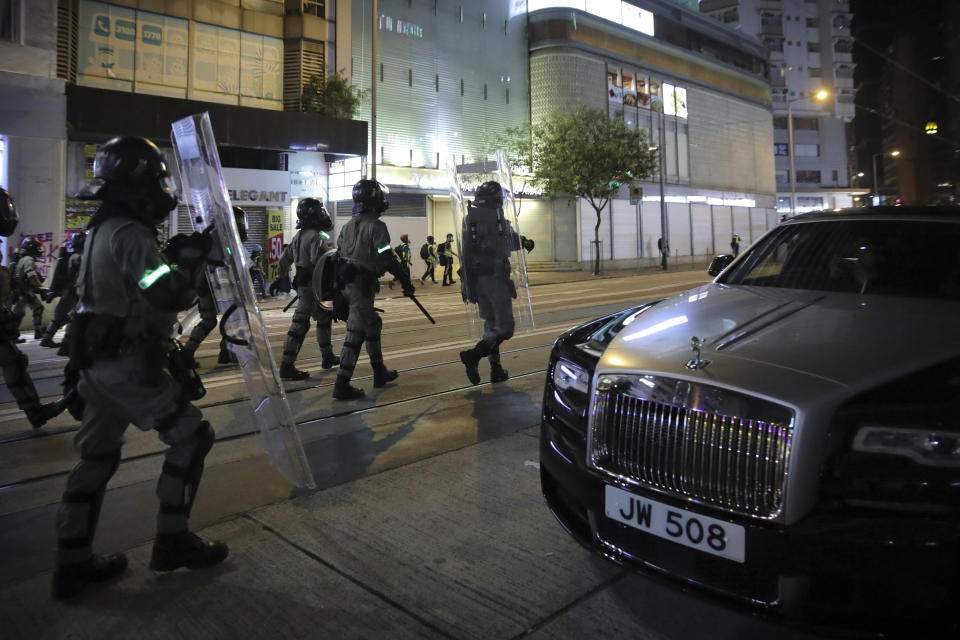 Police officers in riot gear move past a parked Rolls Royce automobile during a protest in Hong Kong, Saturday, Nov. 2, 2019. Pro-democracy protesters attacked the office of Chinese news agency Xinhua for the first time Saturday, after familiar chaos downtown that saw police and demonstrators trading petrol bombs, tear gas and water cannon in the 22nd straight weekend of unrest. (AP Photo/Kin Cheung)
