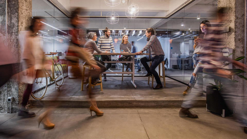 Happy entrepreneur having a business meeting inside of an office while their colleagues are walking in blurred motion.