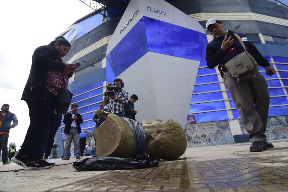 In this Jan. 13, 2020 photo, members of the media take images of a destroyed bust of Bolivia's former President Evo Morales, after it was knocked down on the orders of Bolivia's sports minister, outside a sports center in Cochabamba, Bolivia. Across Bolivia, the government of interim President Jeanine Áñez is taking down statues, painting over murals, changing the names of soccer fields and stadiums, and trying to erase the legacy of the former leader, who ruled the Andean country for more than 14 years as its first indigenous president. (Daniel James/Los Tiempos via AP)