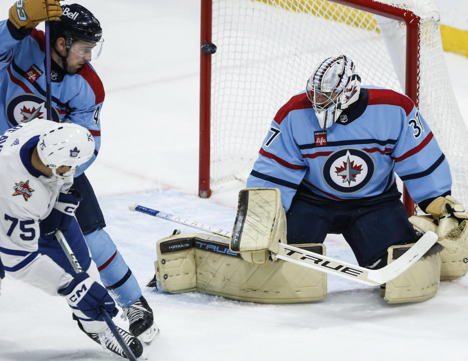 Winnipeg Jets' Neal Pionk (4) defends as Toronto Maple Leafs' Ryan Reaves (75) scores on goaltender Connor Hellebuyck (37) during the first period of an NHL hockey game, Saturday, Jan. 27, 2024, in Winnipeg, Manitoba. (John Woods/The Canadian Press via AP)