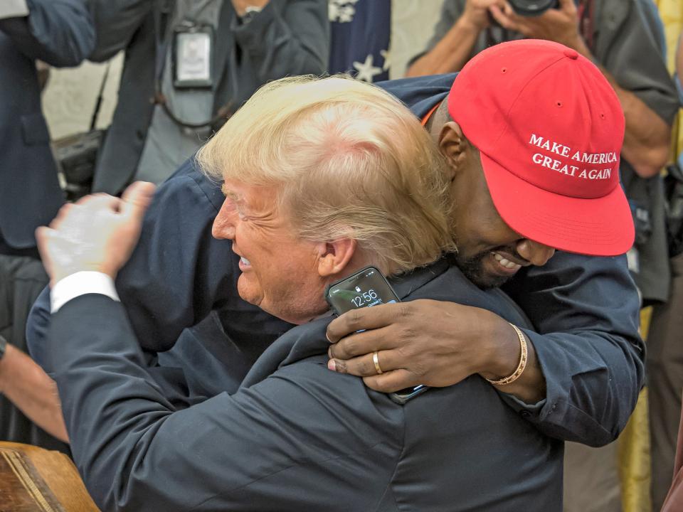 Kanye West, in a red MAGA hat, hugs DOnald Trump in the Oval Office.