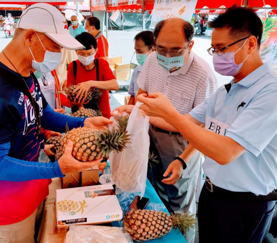 市府農業局農務科長許文耀（中）、關廟區農會推廣部主任黃國斌（右），出席十四農會聯合物產展，親自上場賣鳳梨。（記者羅玉如攝）