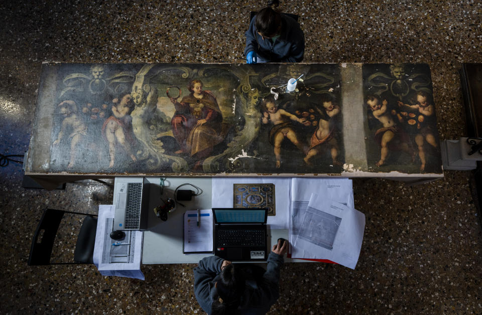 Restorers Annalisa Tosatto, bottom, and Alice Chiodelli work at the conservation and study of ' The reward and a pair of putti', a 1590 painting by Venetian Renaissance artist Andrea Michieli known as Andrea Vicentino in a makeshift laboratory set up in the Venetian Doge's private chapel inside Palazzo Ducale in Venice, northern Italy, Wednesday, Dec. 7, 2022. The 93x330 centimeters (approximately 36.6x130 inches) canvas was adorning the Grimani's Hall in the Doge's apartments of Palazzo Ducale. (AP Photo/Domenico Stinellis)