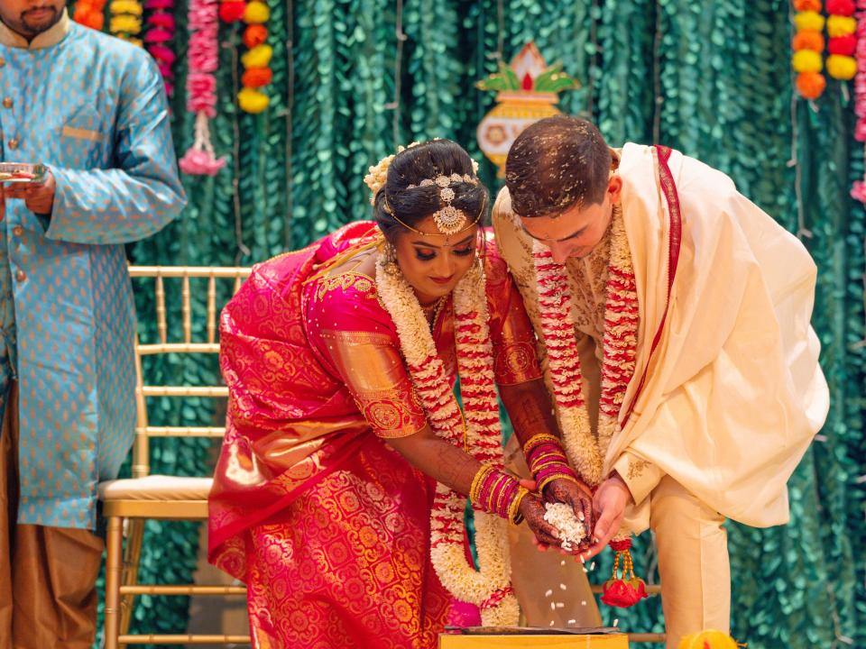 The couple are undertaking a Telegu Hindu wedding ceremony, wearing traditional Indian clothing and standing in front of a green and yellow backdrop.