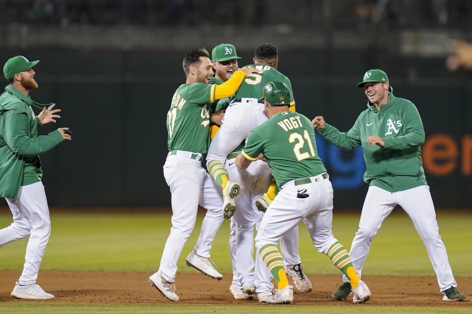 Oakland Athletics' Chad Pinder (obscured) is congratulated by teammates after grounding into a force out and reaching first safely on a throwing error by New York Yankees second baseman DJ LeMahieu, driving in the winning run in the 11th inning of a baseball game in Oakland, Calif., Saturday, Aug. 27, 2022. (AP Photo/Godofredo A. Vásquez)