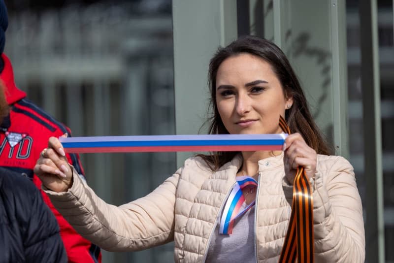 A woman holds a ribbon in the colors of the Russian flag in front of the Consulate General during the 2024 Russian presidential elections. Thomas Banneyer/dpa