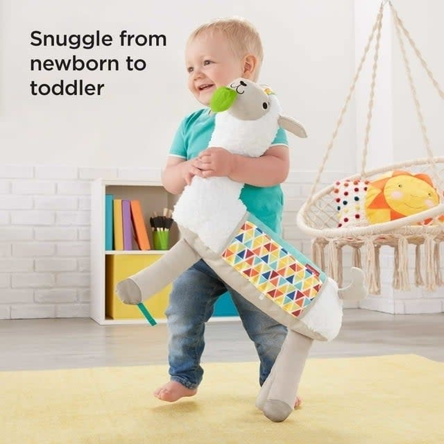 Toddler hugging a plush sheep toy with a patterned body, in a playroom setting. Advert for a transitional snuggle toy