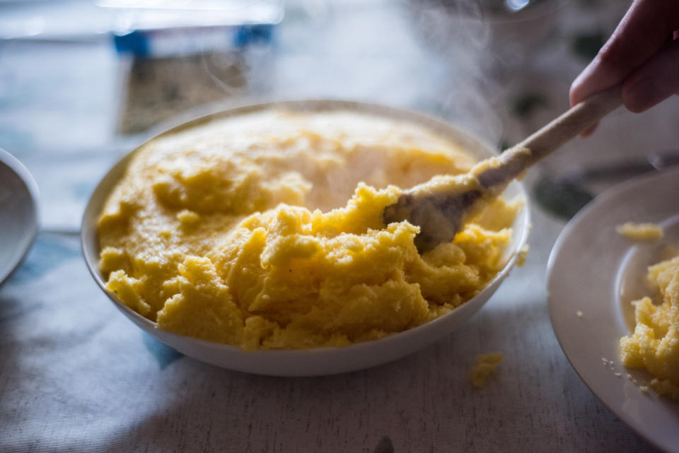 Close up of a wooden spoon serving polenta.