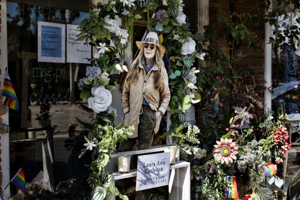 A photo of store owner Laura Ann Carleton is surrounded by flowers and Pride flags and placed on a memorial outside her store in the Studio City section of Los Angeles, Wednesday, Aug. 23, 2023. Authorities say a 27-year-old man was killed by California sheriff's deputies over the weekend after he fatally shot Carleton, outside her store in Cedar Glen, Calif., roughly 60 miles (96 kilometers) east of downtown Los Angeles. Investigators determined that prior to the shooting the suspect tore down a Pride, or rainbow, flag that was hanging in front of the store and yelled many homophobic slurs toward Carleton. (AP Photo/Richard Vogel)