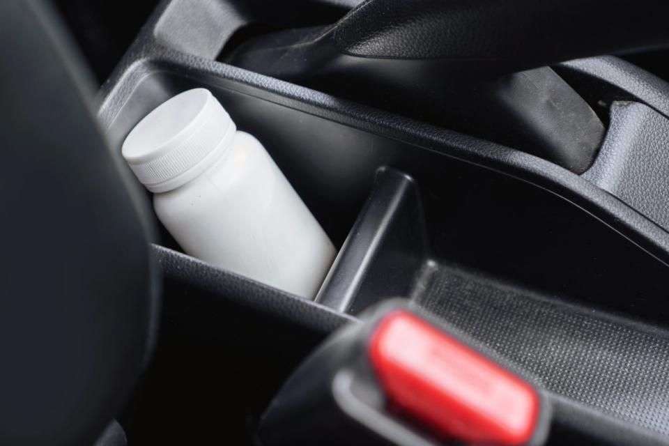 White bottle of medicine in a car's storage console next to the emergency brake.