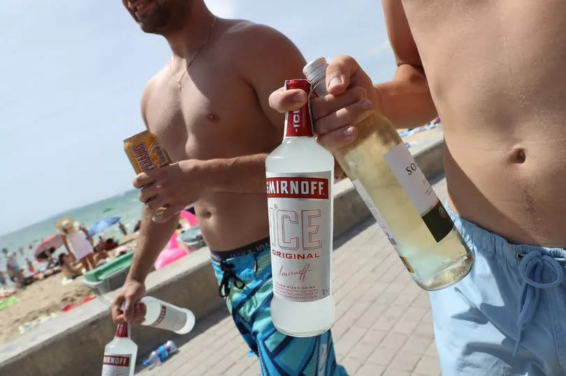 Two young men carry bottles of alcohol they just bought, including Smirnoff Ice, to the beach at the Ballermann stretch on July 26, 2017 in Palma de Mallorca, Spai