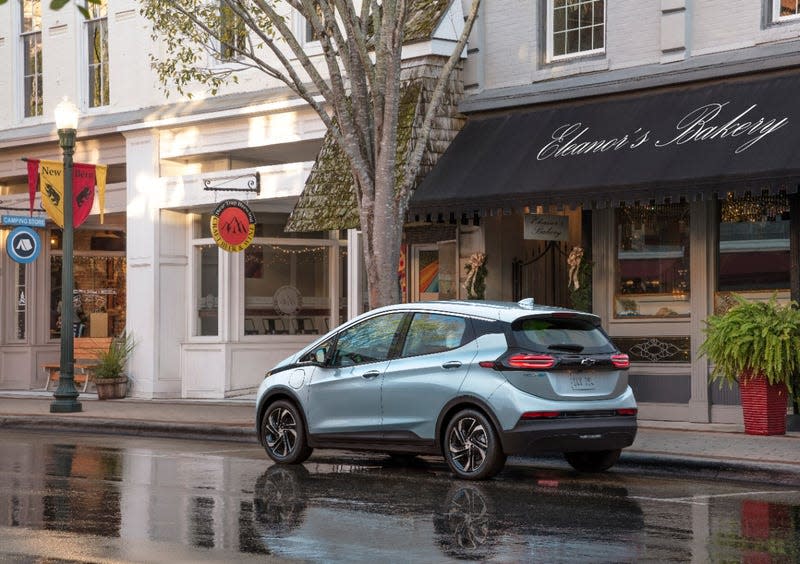 A Chevy Bolt parked on a rainy road in front of some shops