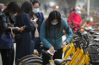 A woman wearing a face mask to help curb the spread of the coronavirus uses an alcohol tissue to disinfect a bicycle of bike-sharing companies during the morning rush hour in Beijing, Monday, Oct. 26, 2020. Schools and kindergartens have been suspended and communities are on lockdown in Kashgar, a city in China's northwest Xinjiang region, after more than 130 asymptomatic cases of the coronavirus were discovered. (AP Photo/Andy Wong)