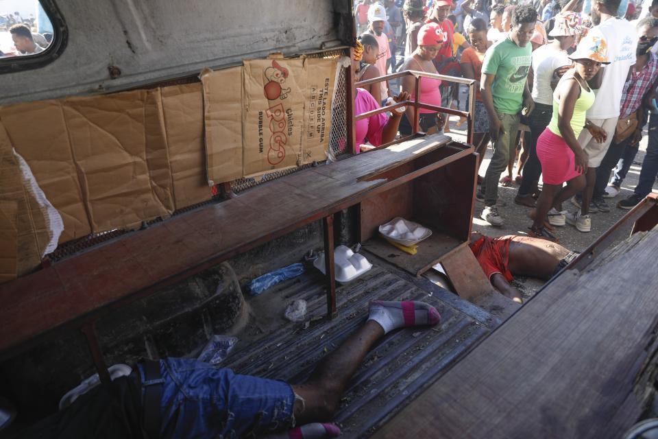 EDS NOTE: GRAPHIC CONTENT - A body lies inside a taxi, left, and another on the ground behind, after an overnight shooting in the Petion Ville neighborhood of Port-au-Prince, Haiti, Monday, March 18, 2024. (AP Photo/Odelyn Joseph)