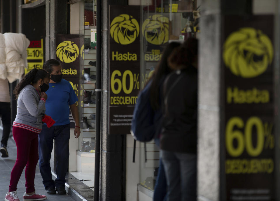 Shoppers look into a store announcing discounts in downtown Mexico City, Friday, Oct. 30, 2020. Prior to the coronavirus pandemic, Mexico’s economy was in recession, and that only deepened with the economic shutdown provoked by measures aimed at slowing the spread of COVID-19 during the second quarter. (AP Photo/Fernando Llano)