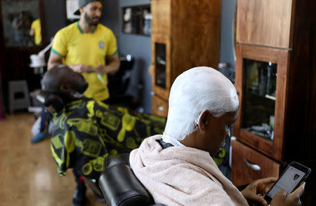 FILE PHOTO: A client looks at his mobile phone before getting shaved at the Bespoken Man, a full-service gentleman's barber shop in Sandton, South Africa, December 14, 2018. REUTERS/Siphiwe Sibeko